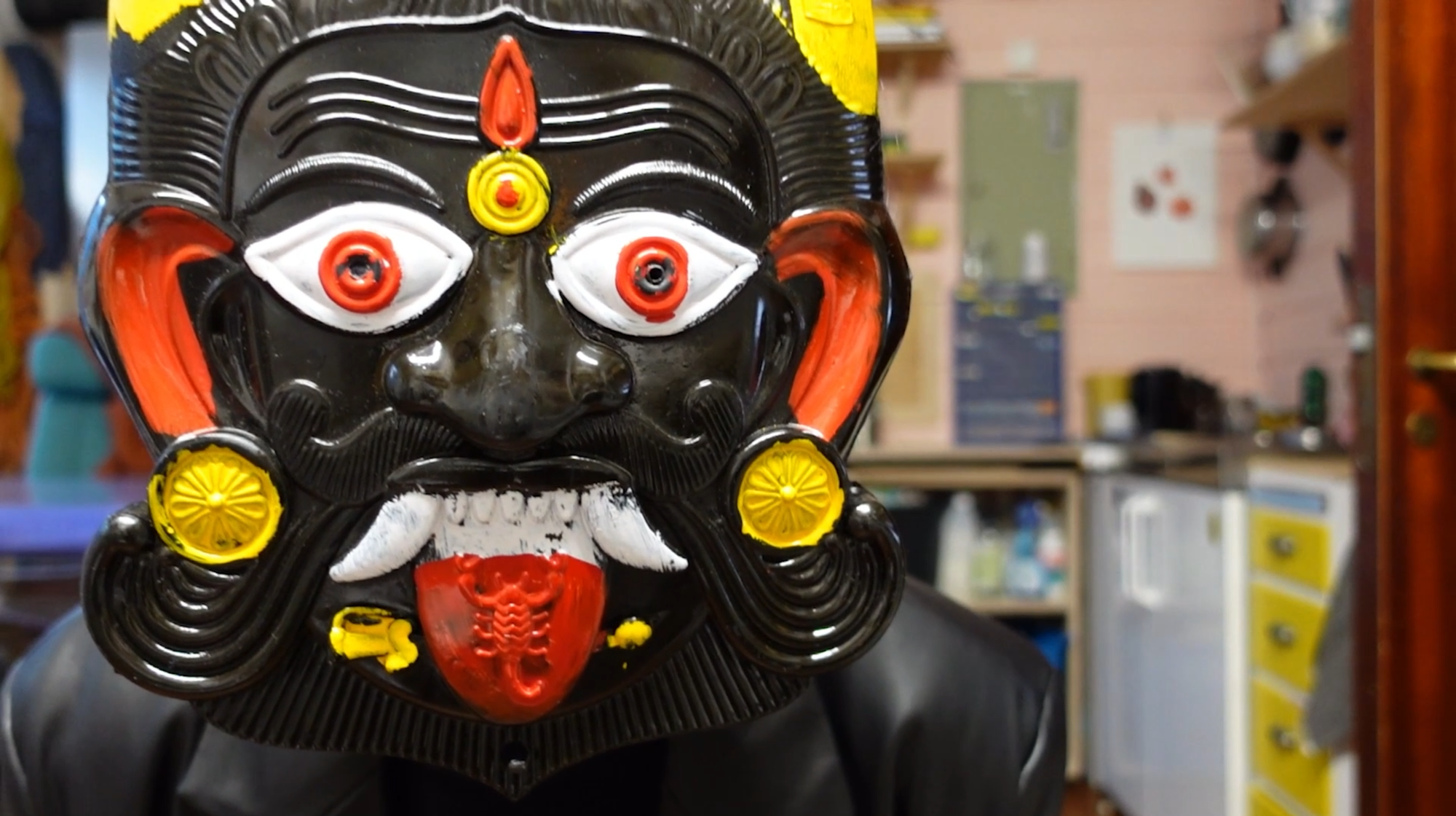 Fargefoto av en svart maske med gule, røde og hvite detaljer.