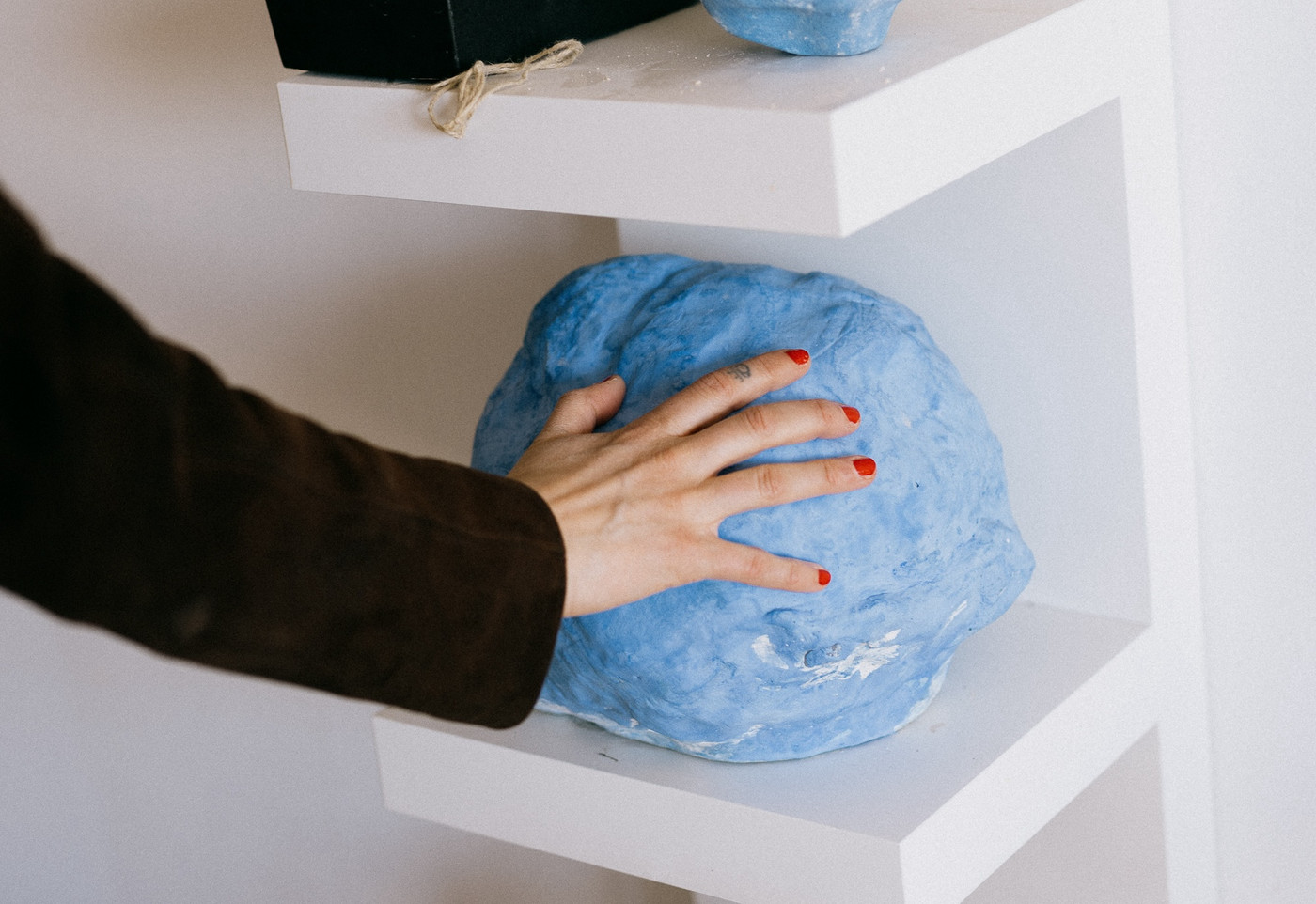 Photo showing a hand with red nailpolish touching a blue, round, sculpture made by artist Kachun Lay.