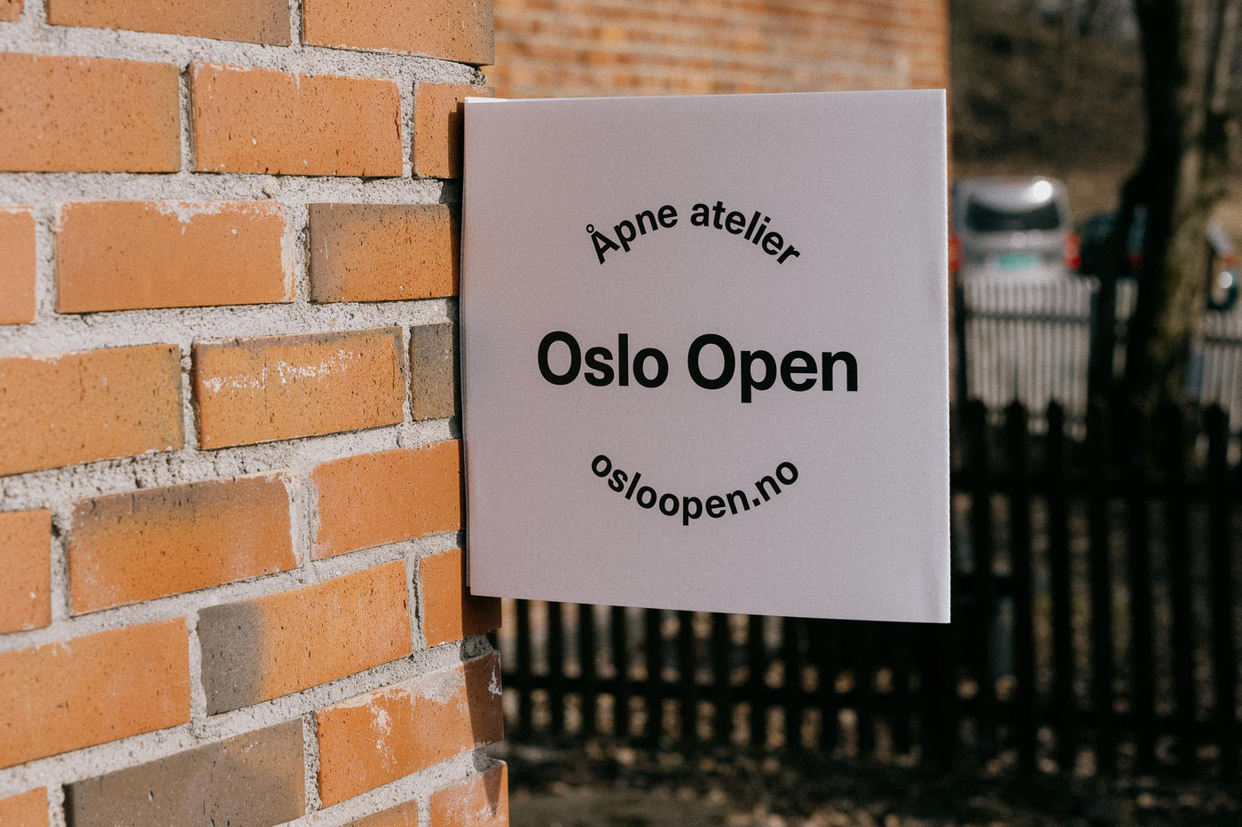 A white sign reading "Åpne atelier - Oslo Open" hanging from a brick wall.