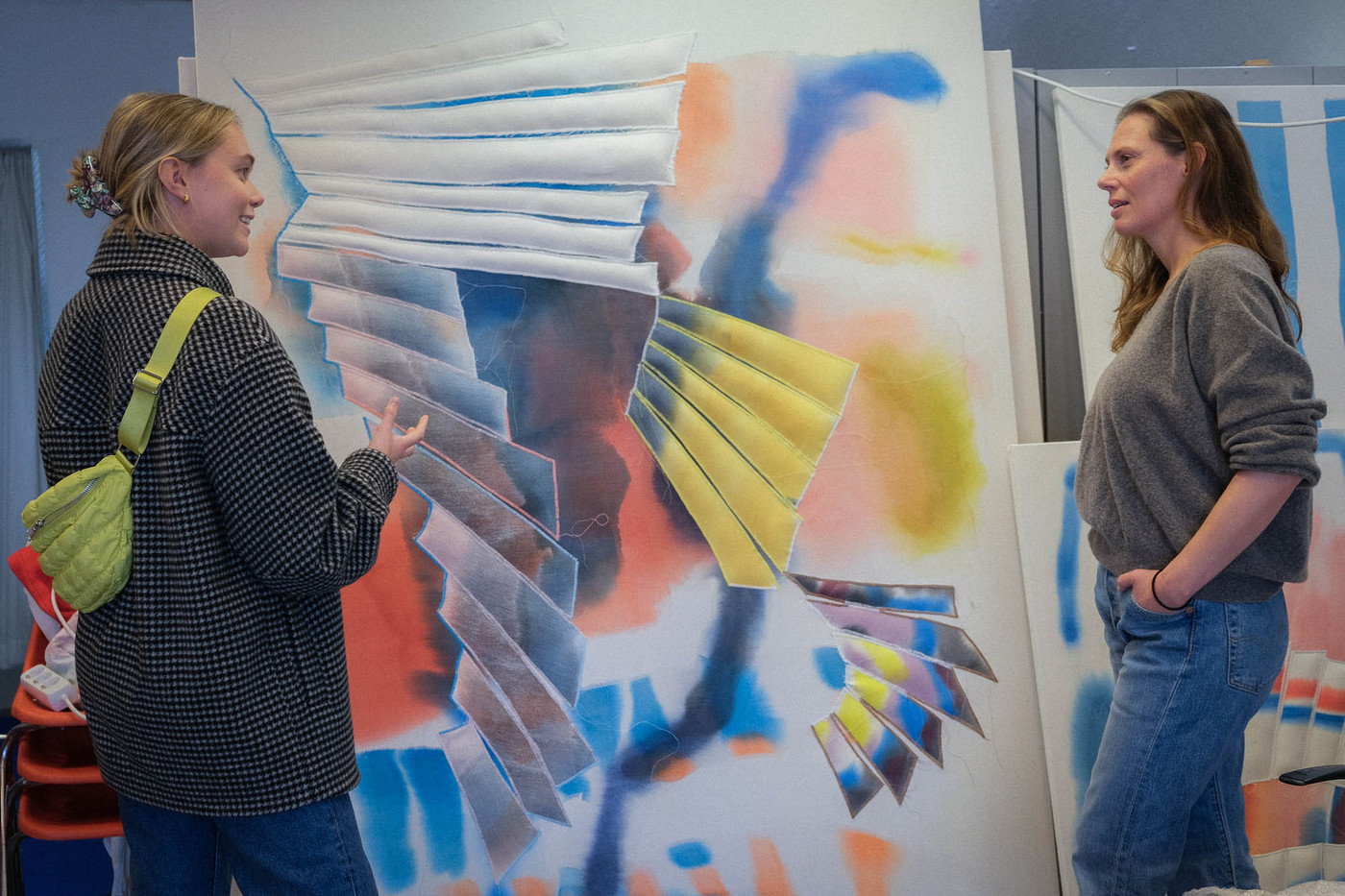 Marie Saxeide og kunstner Liv Tandrevold Eriksen snakker sammen foran et stort og fargerikt kunstverk som står lent opp mot en vegg.