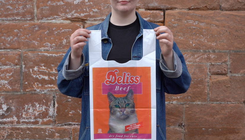 Artist holding up a plastic bag to camera displaying a photograph of a cat with advert for cat food