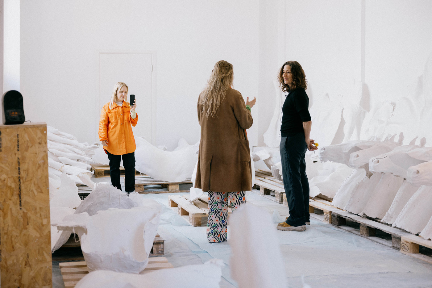 Marthe Elise Stramrud filmer en samtale mellom reporter Ragnhild Brochmann og kunstner Vibeke Tanberg på mobiltelefonen. Rundt dem ligger det gipsavstøpninger av hestehoder.