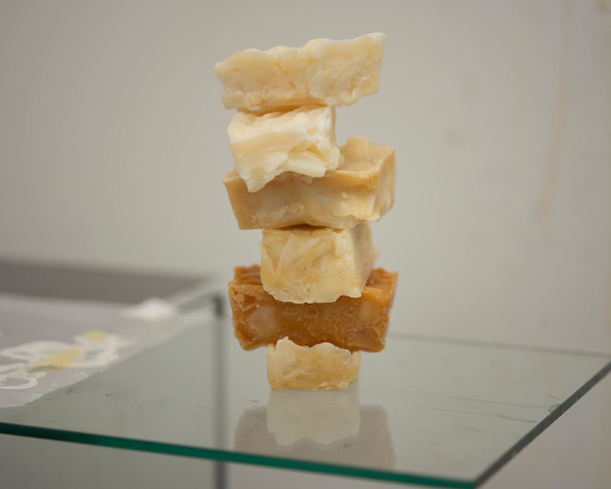 A tower of six handmade soap bars in beige and brown stand on a square of glass 