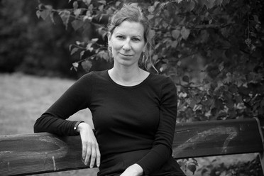 Et svart-hvitt portett av en kvinne med lyst hår og hud. Hun sitter på en parkbenk og ser rett i kamera.