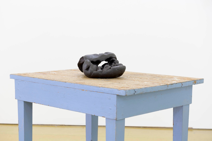 Liten sort skulptur på gammelt blå bord. Keramikken ser ut som en klump med ubrent leire