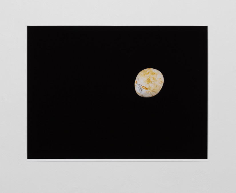 Image from exhibition showing a rectangular black photograph with an apparently floating circular shape which is in reality a small stone, but reminiscent of a planet against the black background of the universe.