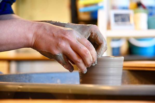 A close up of hands throwing clay on a pottery wheel